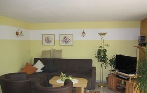 Uma sala de estar com sofá, duas poltronas, uma mesa de centro, um rack para TV e uma planta.