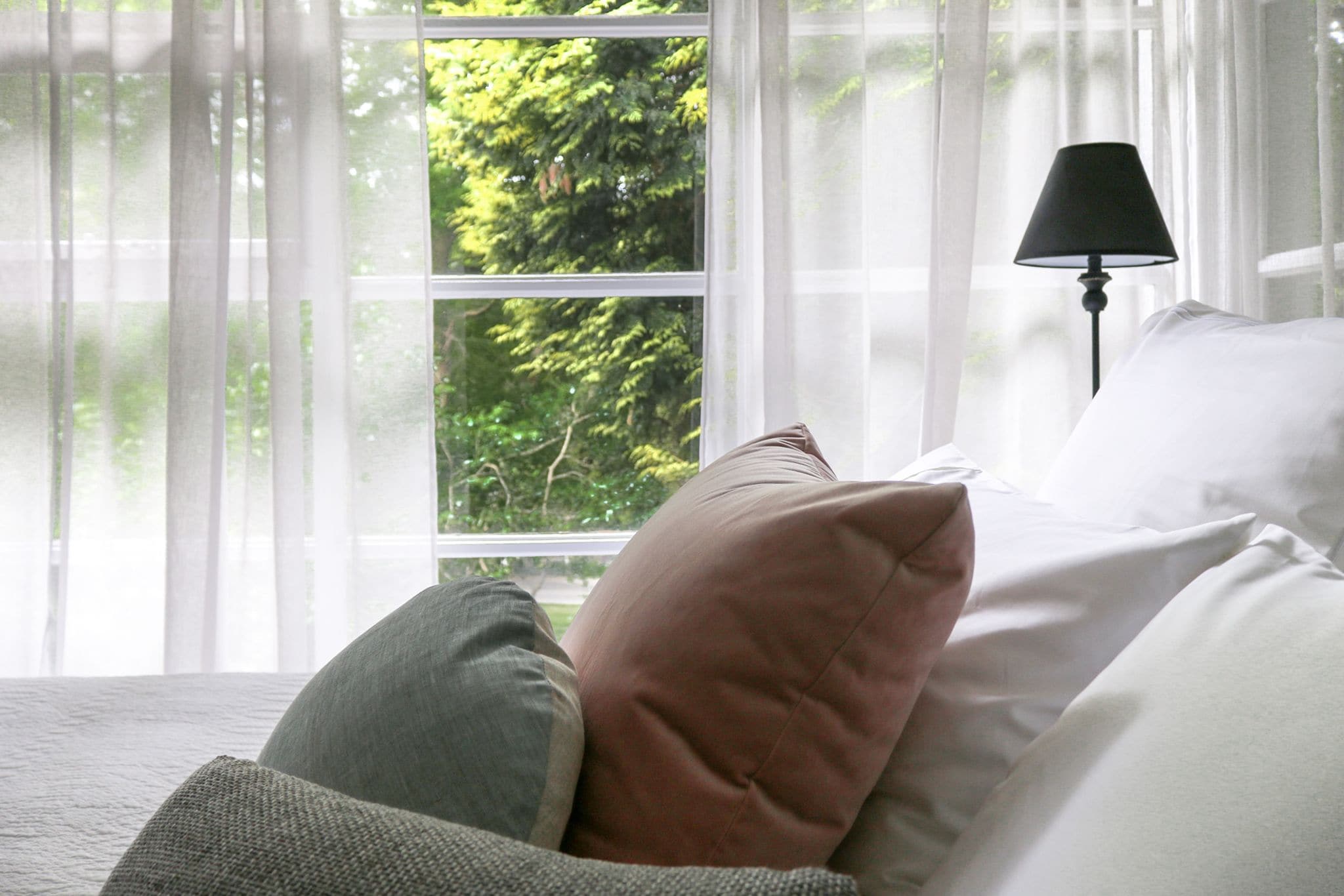 A bedroom with a bed, pillows, a lamp, and a window with curtains.