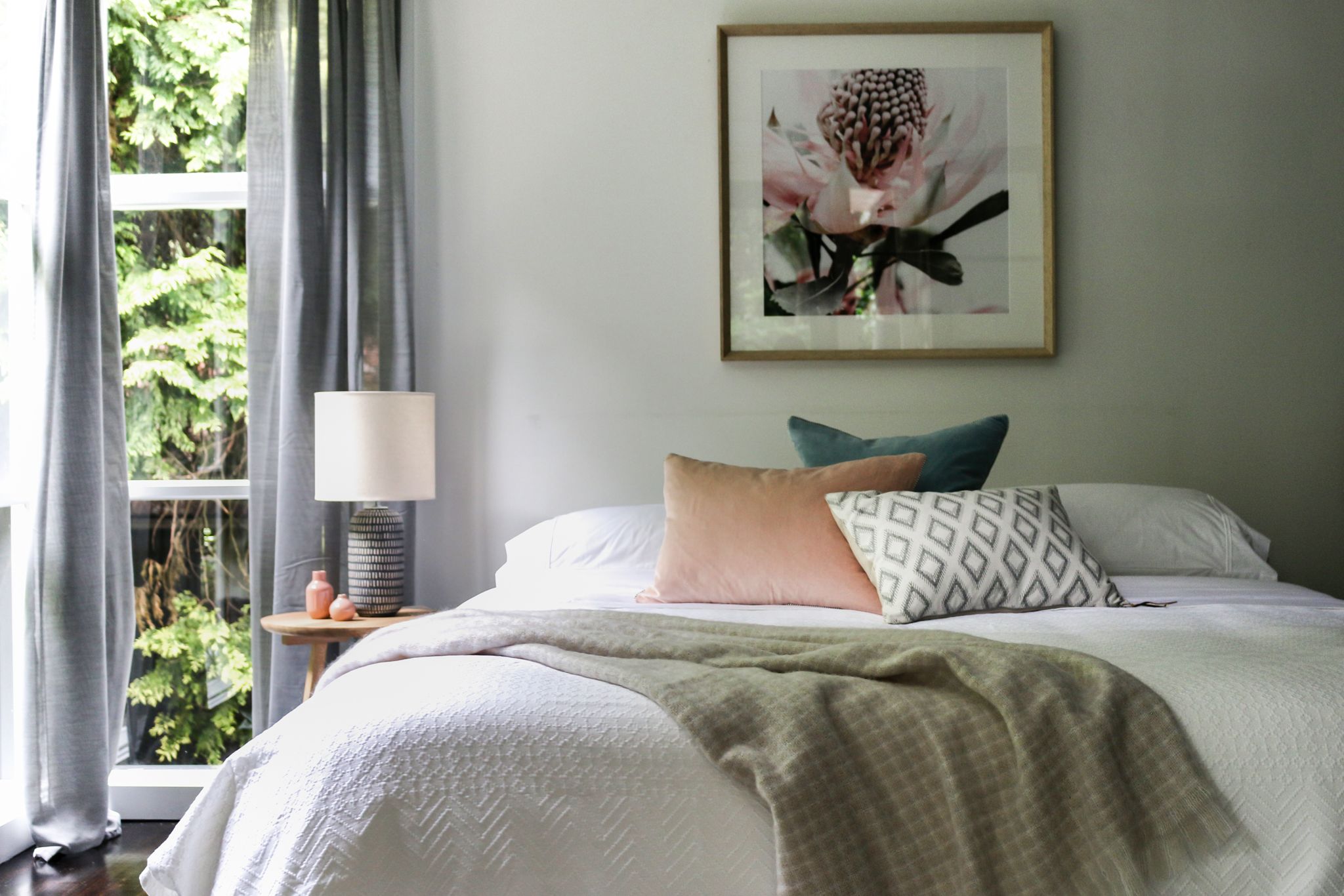 A bedroom with a bed, pillows, a bedside table with a lamp, and a framed picture on the wall.