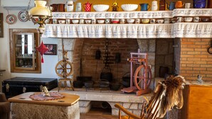 Cocina rústica con chimenea de ladrillo, mobiliario de madera y una variedad de utensilios de cocina en estantes sobre la chimenea.