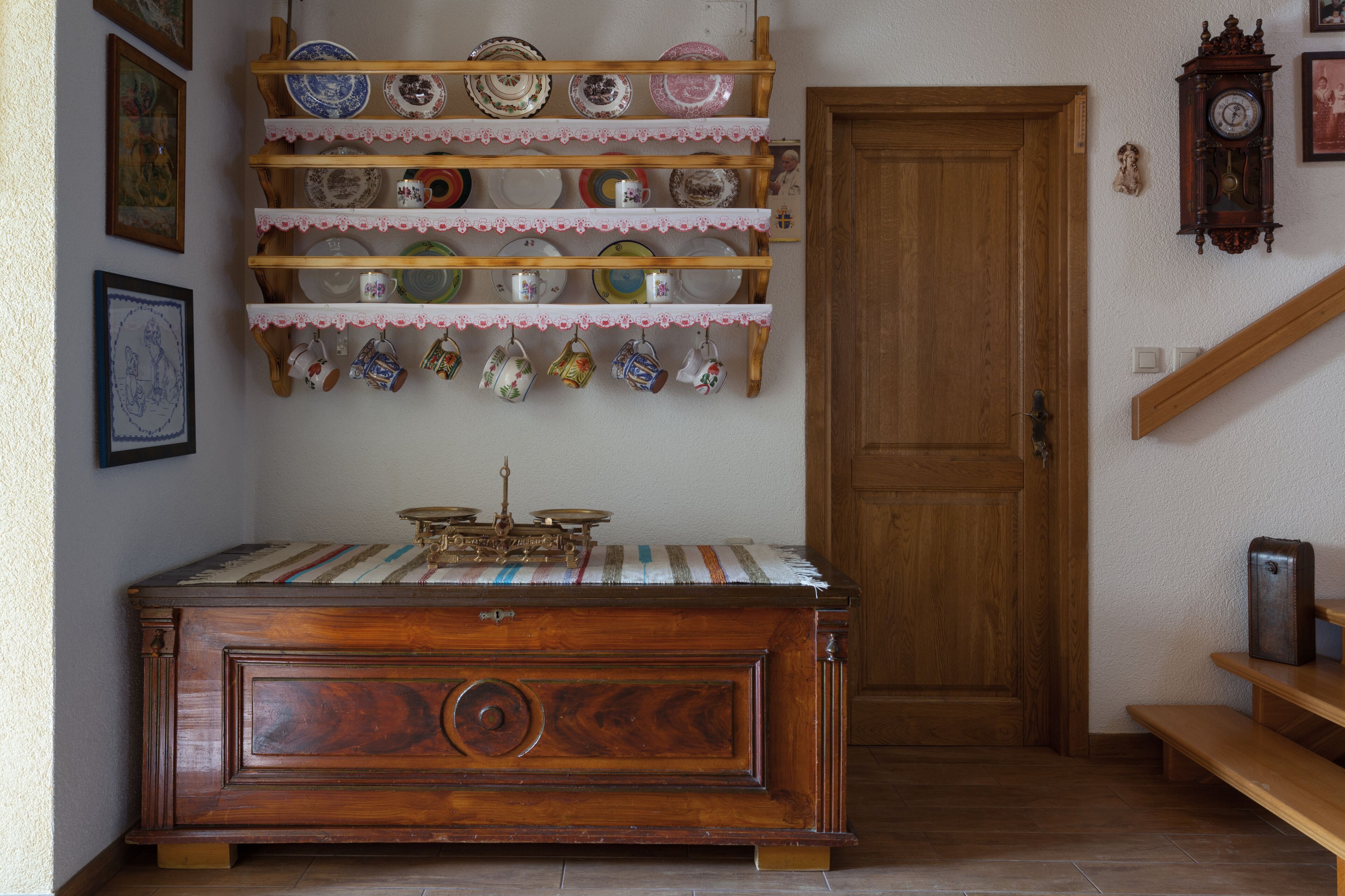 A wooden cabinet with a clock, a shelf with dishes, and a door in a room.