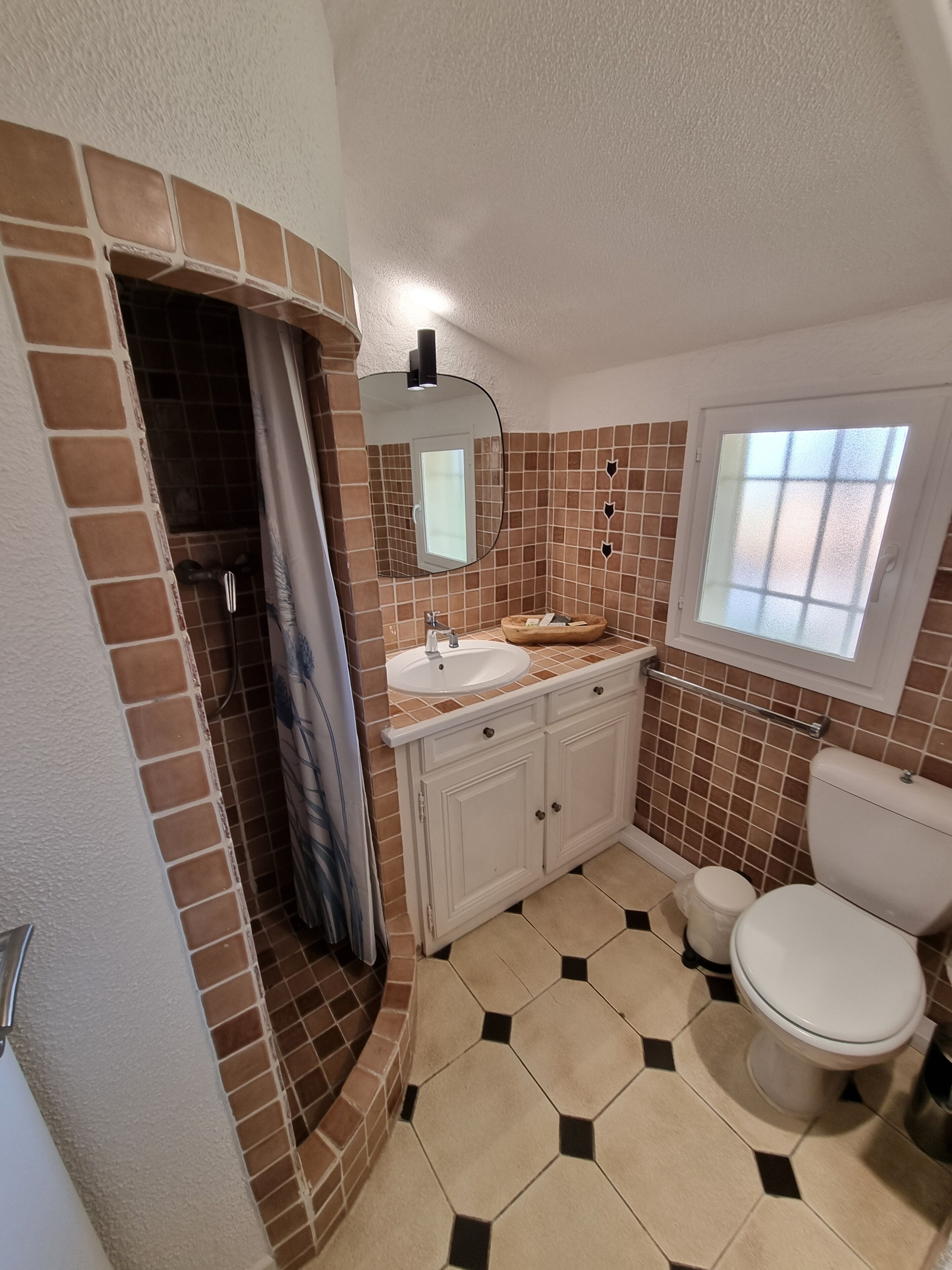 A bathroom with a shower, toilet, sink, and a window.