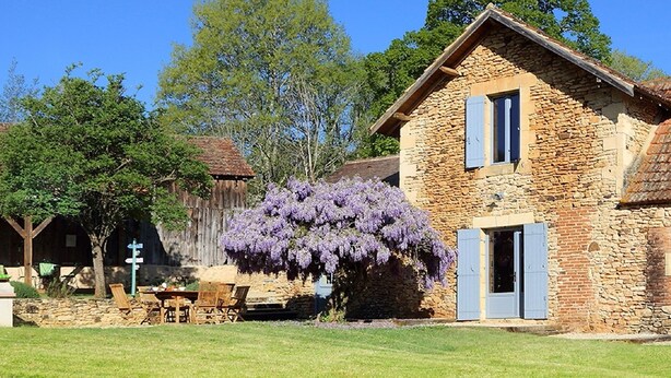 A rustic stone building with a wooden porch and a table with chairs. - GITE SAINT-AMAND AT FELICIE (Le Bugue)