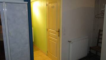 Un couloir avec une porte donnant sur une pièce, un radiateur et une chaise.