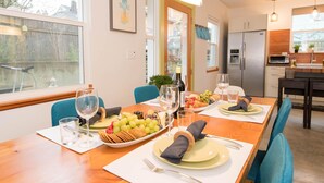 Un coin repas avec une table en bois dressée pour quatre personnes, agrémentée d’un plateau de fruits, de verres à vin et d’assiettes.