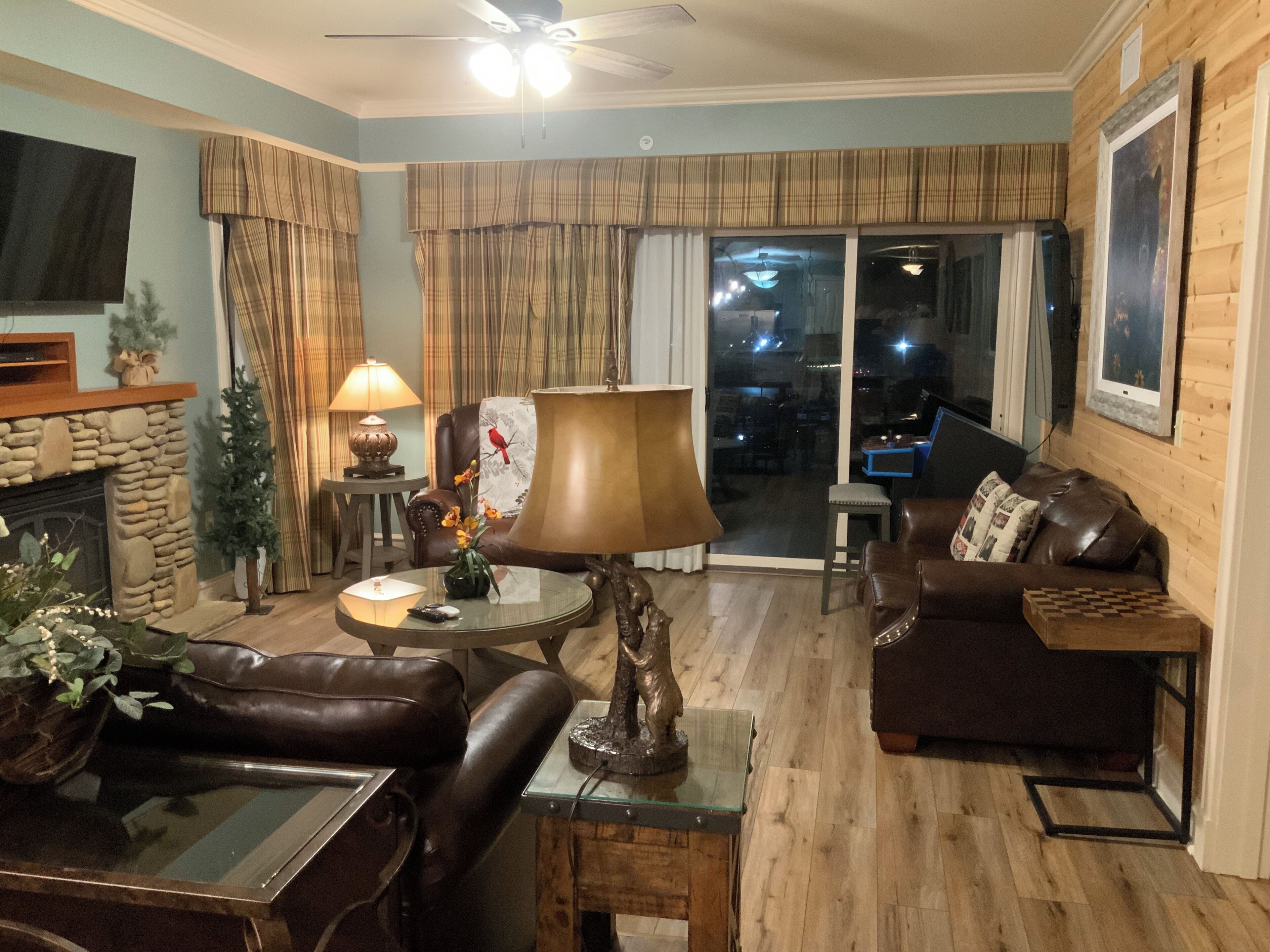 A living room with a fireplace, leather sofas, a coffee table, and a large window with a view of the city at night.