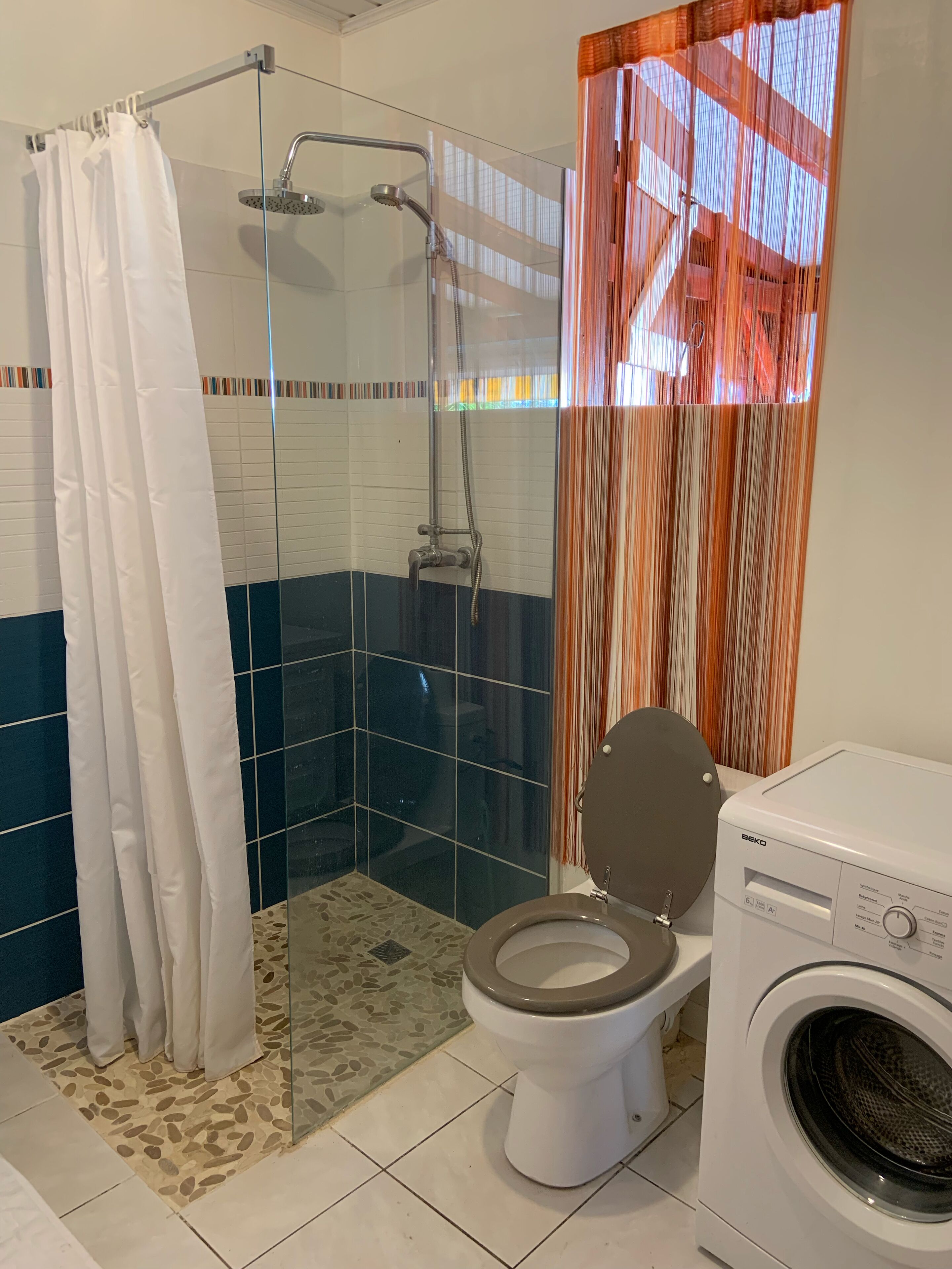 Un baño con ducha de vidrio, inodoro y lavadora.