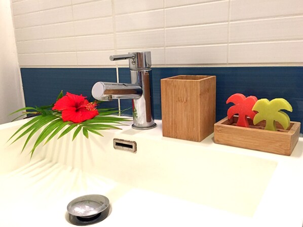 Un lavamanos con grifo moderno, una caja de madera con objetos decorativos con forma de palmera y una flor de hibisco rojo.
