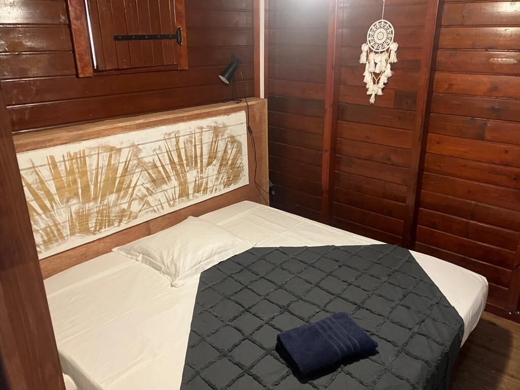 A wooden cabin-style room with a bed, a headboard with a nature-themed design, a dreamcatcher, and a small lamp.