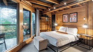 Un dormitorio moderno con una cama grande, un pequeño espacio para sentarse y vistas a través de amplios ventanales.