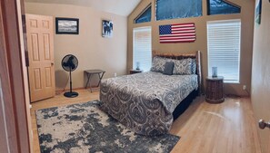 Ein Schlafzimmer mit einem Bett, einem Ventilator, einem Teppich, einem kleinen Tisch und einer US-amerikanischen Flagge an der Wand.