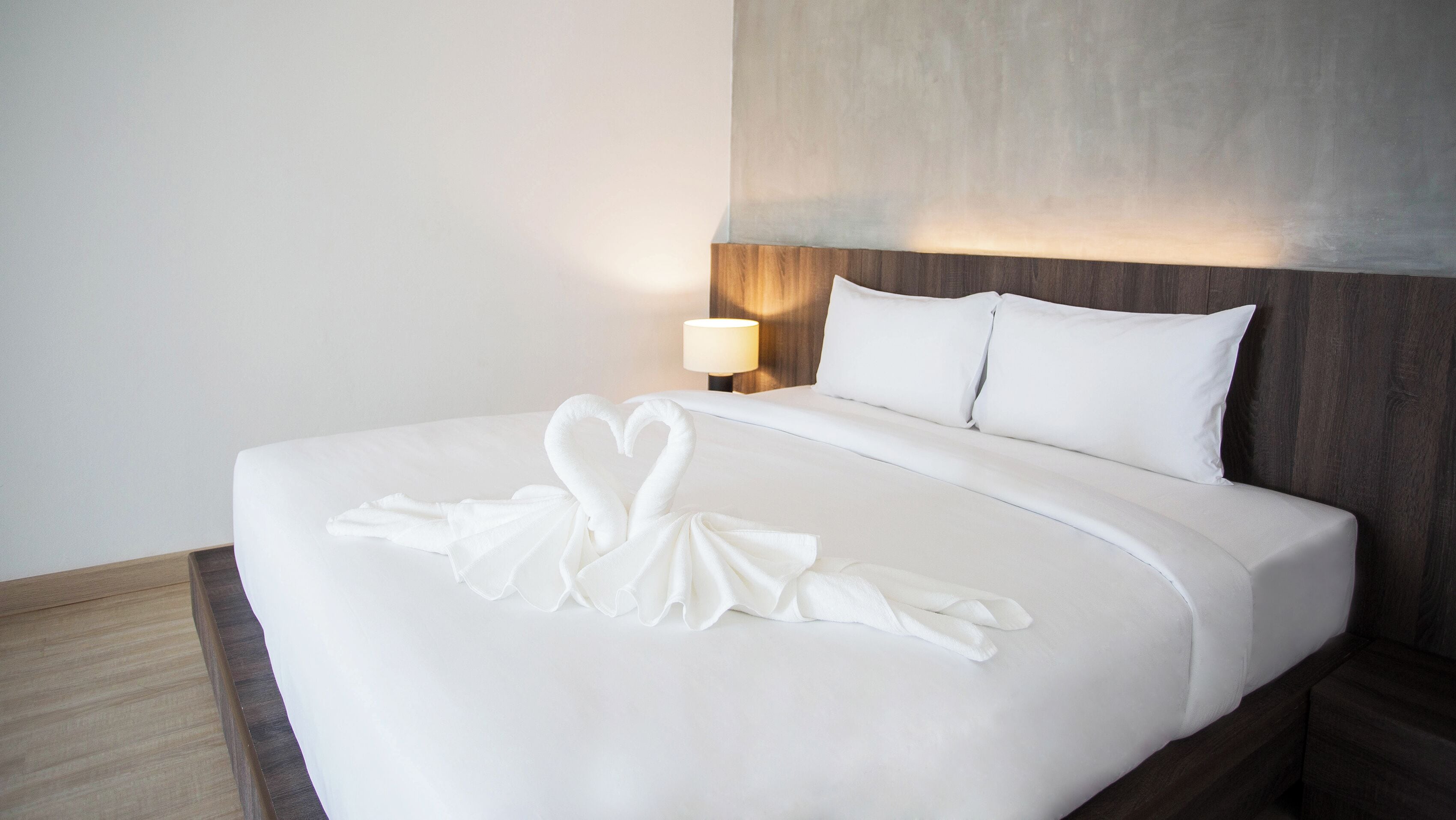 Een hotelkamer met een net opgemaakt bed, een houten hoofdeinde en een bedlampje.
