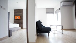A modern hotel room with a bed, a chair, a small table, and a TV mounted on the wall.