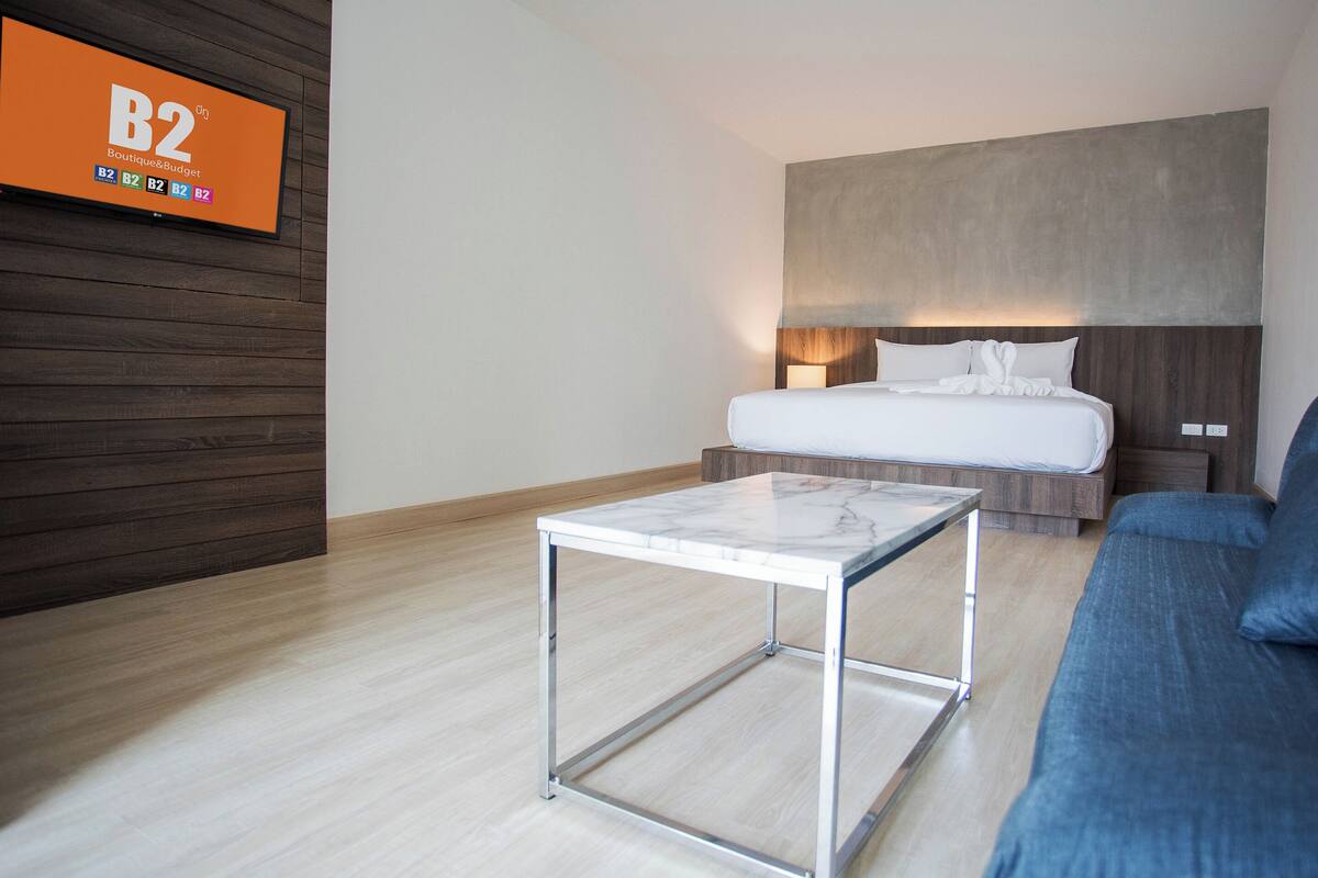 Een hotelkamer met een bed, een blauwe sofa, een marmeren tafel en een televisie waarop 'B2 Boutique & Budget' staat.