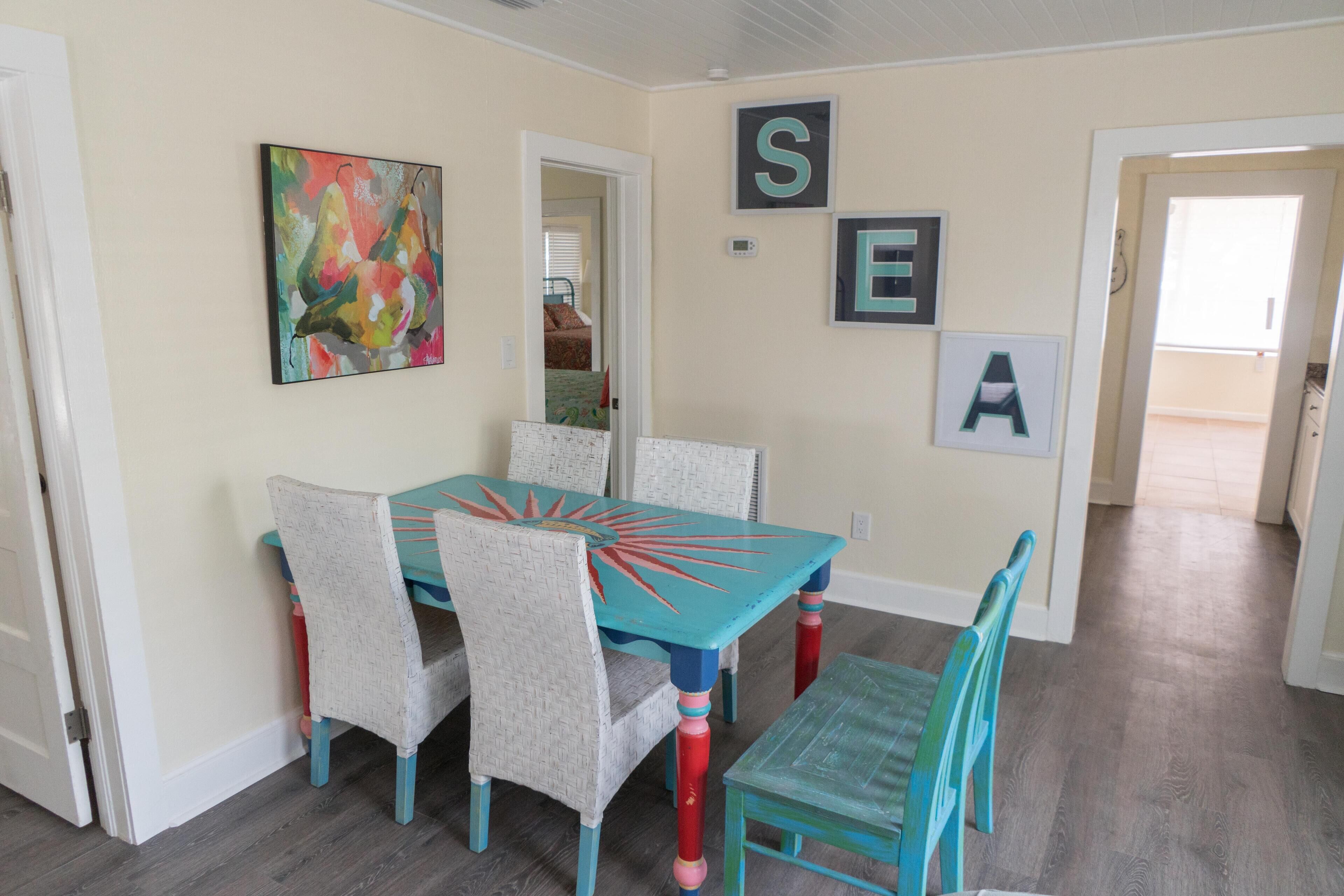 A dining area with a turquoise table and chairs, a colorful abstract painting, and alphabet letters on the wall.