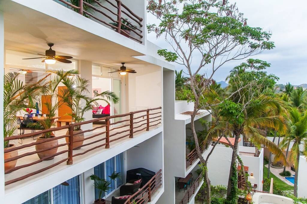 A multi-story hotel with balconies, outdoor seating, and lush greenery.