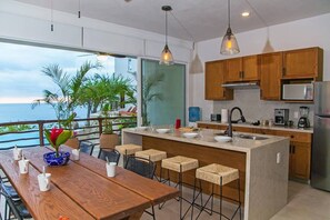 Enjoy ocean views from the kitchen and dining area, featuring a spacious kitchen with a sink, coffee maker, and blender, and a dining table with chairs and a stool.