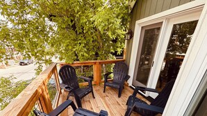 Eine Holzterrasse mit vier schwarzen Adirondack-Stühlen, einem Hollerleger und Blick auf eine Straße und Bäume.