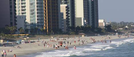 A beach with people and waves, and tall buildings in the background.