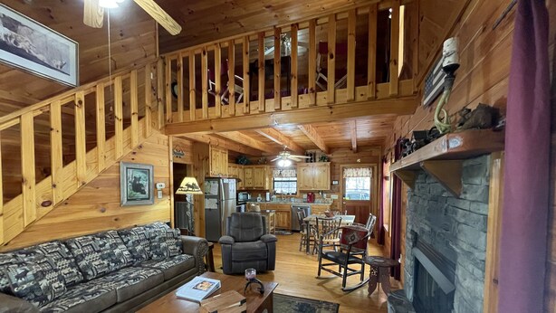 A spacious cabin interior with a wooden staircase, a dining area, a fireplace, and a living room with a sofa and coffee table. - YOUR mountain experience in this luxurious amenity galore cabin in the woods! (Blue Ridge)
