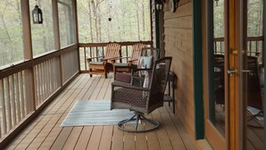 A wooden deck with wicker chairs and a table, overlooking a forested area. - YOUR mountain experience in this luxurious amenity galore cabin in the woods! (Blue Ridge)
