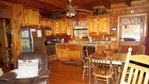 A cabin-style kitchen with wooden cabinets, a refrigerator, microwave, and a dining area with a wooden table and chairs. - YOUR mountain experience in this luxurious amenity galore cabin in the woods! (Blue Ridge)