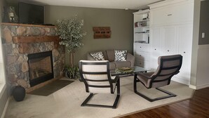 A living room with a stone fireplace, two armchairs, a coffee table, and a bookshelf.