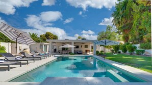 Ein Swimmingpool mit Liegestühlen und Sonnenschirmen, umgeben von einem gepflegten Rasen und Bäumen.