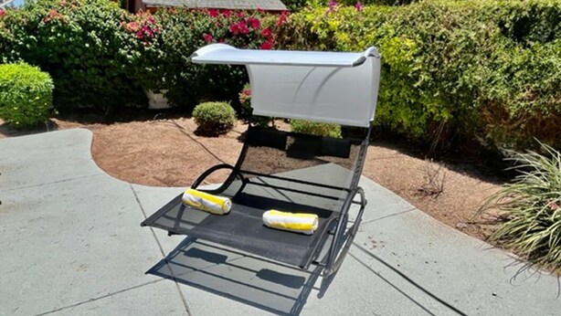 Ein tragbarer Grill mit weißem Bezug und zwei gelben Küchenpapierrollen auf einer Beton-Terrasse.