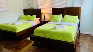 Een hotelkamer met twee bedden, elk met groene beddengoed en witte handdoeken. Er staat een nachtkastje met een lamp tussen de bedden.