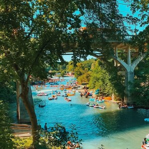 Um rio com vários barcos e pessoas, cercado por árvores e uma ponte.