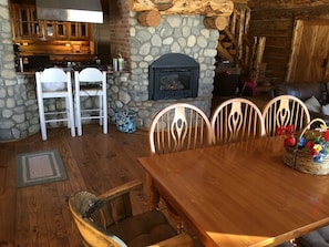 Cozy cabin-style room with a stone fireplace, stove, and wooden dining table.