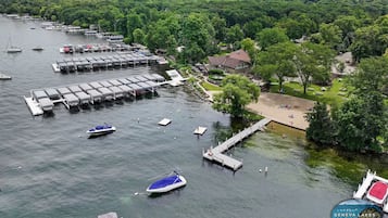 Una marina con barcos amarrados, un muelle que se adentra en el agua y una zona verde con un edificio y árboles.