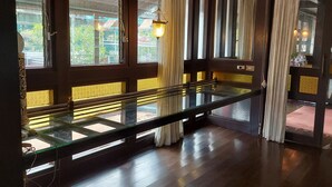 Habitación con un banco de vidrio, suelo de madera y ventanas amplias con cortinas.
