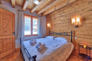 A wooden-paneled room with a bed, two wall-mounted lamps, and a window with curtains.