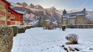 A snow-covered courtyard with buildings, a mountain backdrop, and a clear sky. - Petit Jardin 2 Bed Patio Apt Central Chamonix (Chamonix-Mont-Blanc)