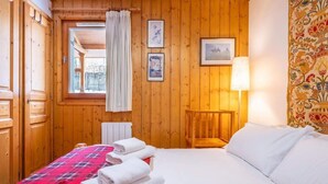 A wooden-paneled room with a bed, a window with curtains, and a lamp. - Petit Jardin 2 Bed Patio Apt Central Chamonix (Chamonix-Mont-Blanc)