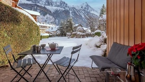 A patio with a table and chairs, a sofa, and a view of snow-covered mountains. - Petit Jardin 2 Bed Patio Apt Central Chamonix (Chamonix-Mont-Blanc)
