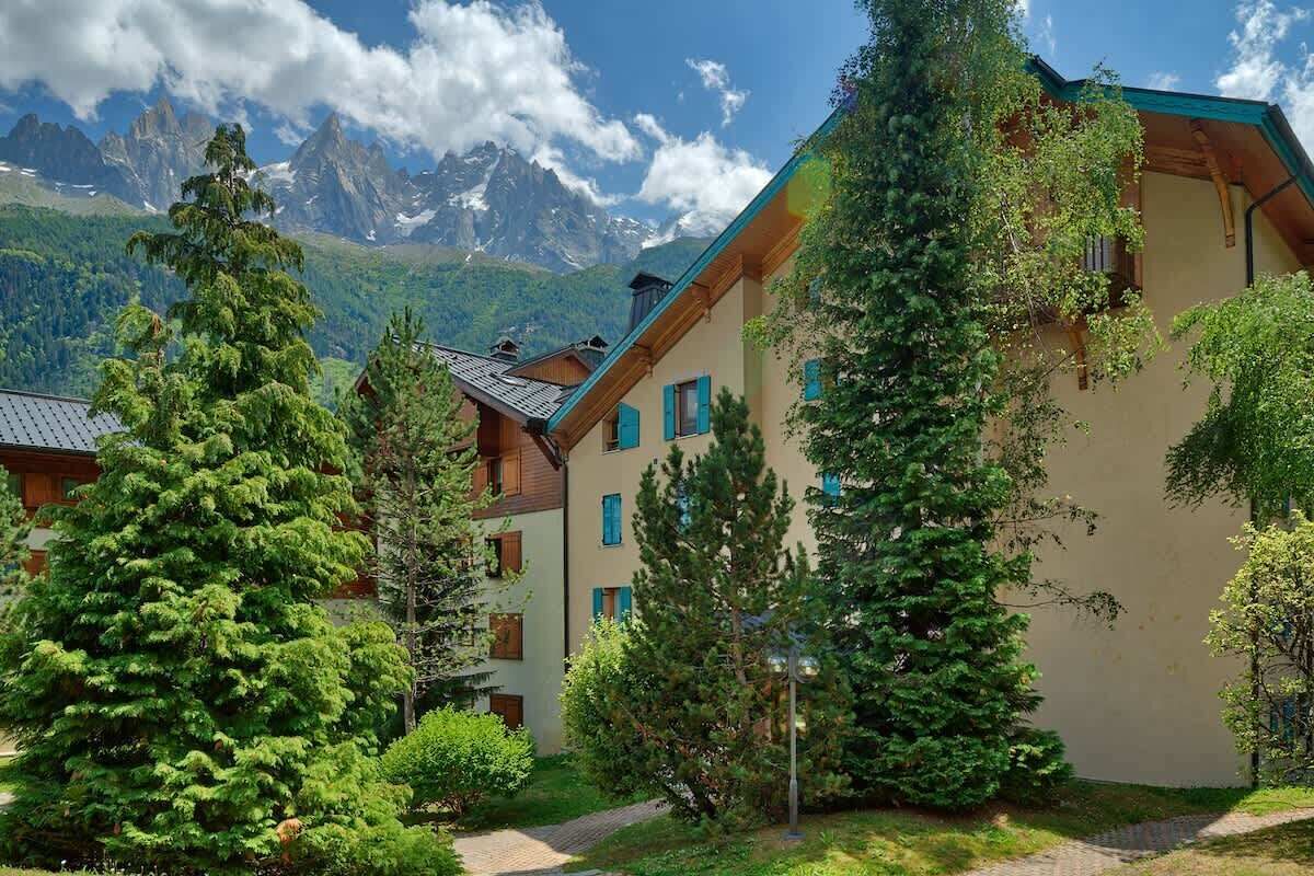 A building with a sloped roof, surrounded by lush greenery and tall trees.