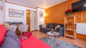 A cozy living room with a red sofa, grey couch, and a wooden TV stand. - Petit Jardin 2 Bed Patio Apt Central Chamonix (Chamonix-Mont-Blanc)