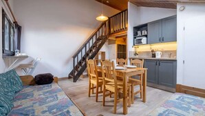 A cozy living room with a sofa, a dining table with chairs, and a staircase leading to an upper level.