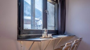 A room with a window overlooking a snowy landscape, a small table with a coffee maker, and a chair.