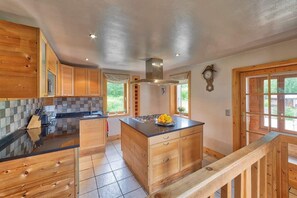 A kitchen with wooden cabinets, a central island, and a view of the outdoors through large windows.