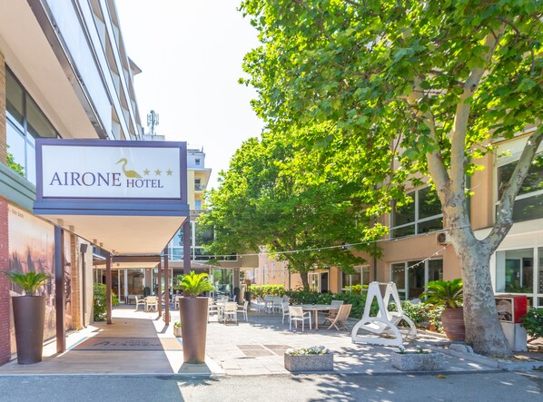 An outdoor seating area with tables and chairs, a large planter, and a sign for the Airone Hotel. - Hotel Airone (Rimini)