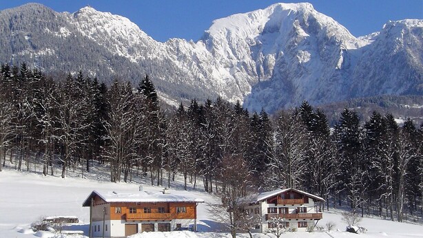 Un chalet à deux étages, doté d’un toit en pente, entouré d’un paysage enneigé et d’une forêt.