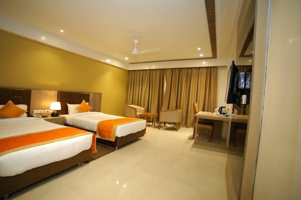 A hotel room with two beds, a desk, a chair, a television, and a ceiling fan.