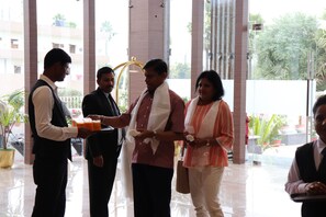 A group of people in a lobby with a glass entrance, potted plants, and a view of buildings outside. - Dhamma Grand Hotel Resort (Gaya)