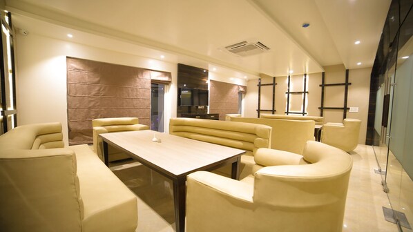 A modern lounge with sofas and a table, a brick accent wall, and a large window. - Dhamma Grand Hotel Resort (Gaya)