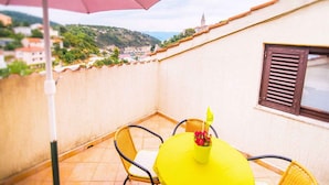 Un balcón con una mesa y sillas, una planta en maceta y vistas a un pueblo y colinas al fondo.