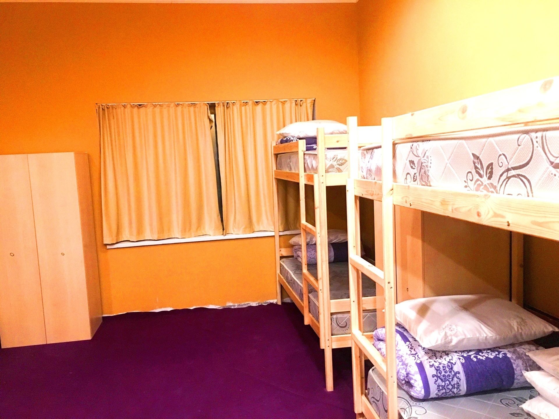 A room with bunk beds, a window with curtains, and a purple carpet.